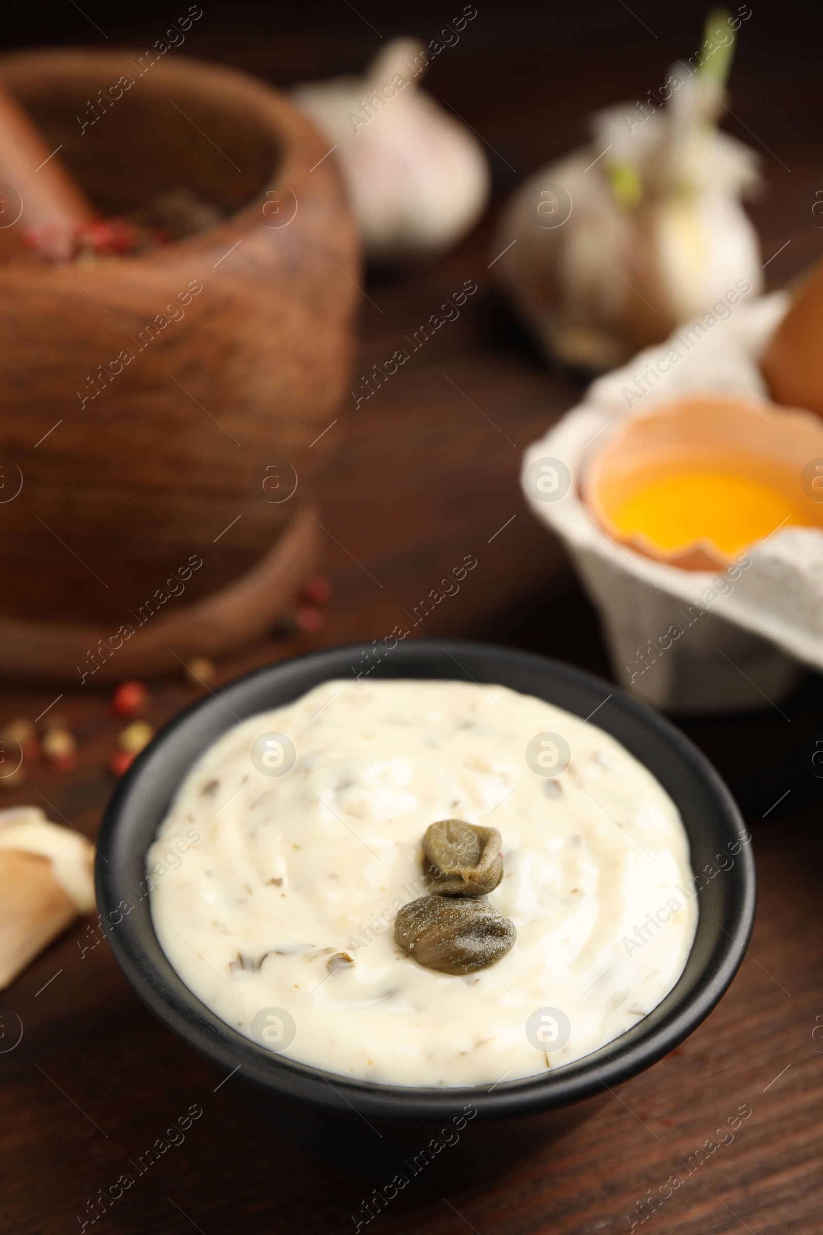 Photo of Creamy caper sauce in bowl on wooden table, closeup