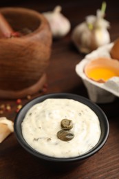 Photo of Creamy caper sauce in bowl on wooden table, closeup