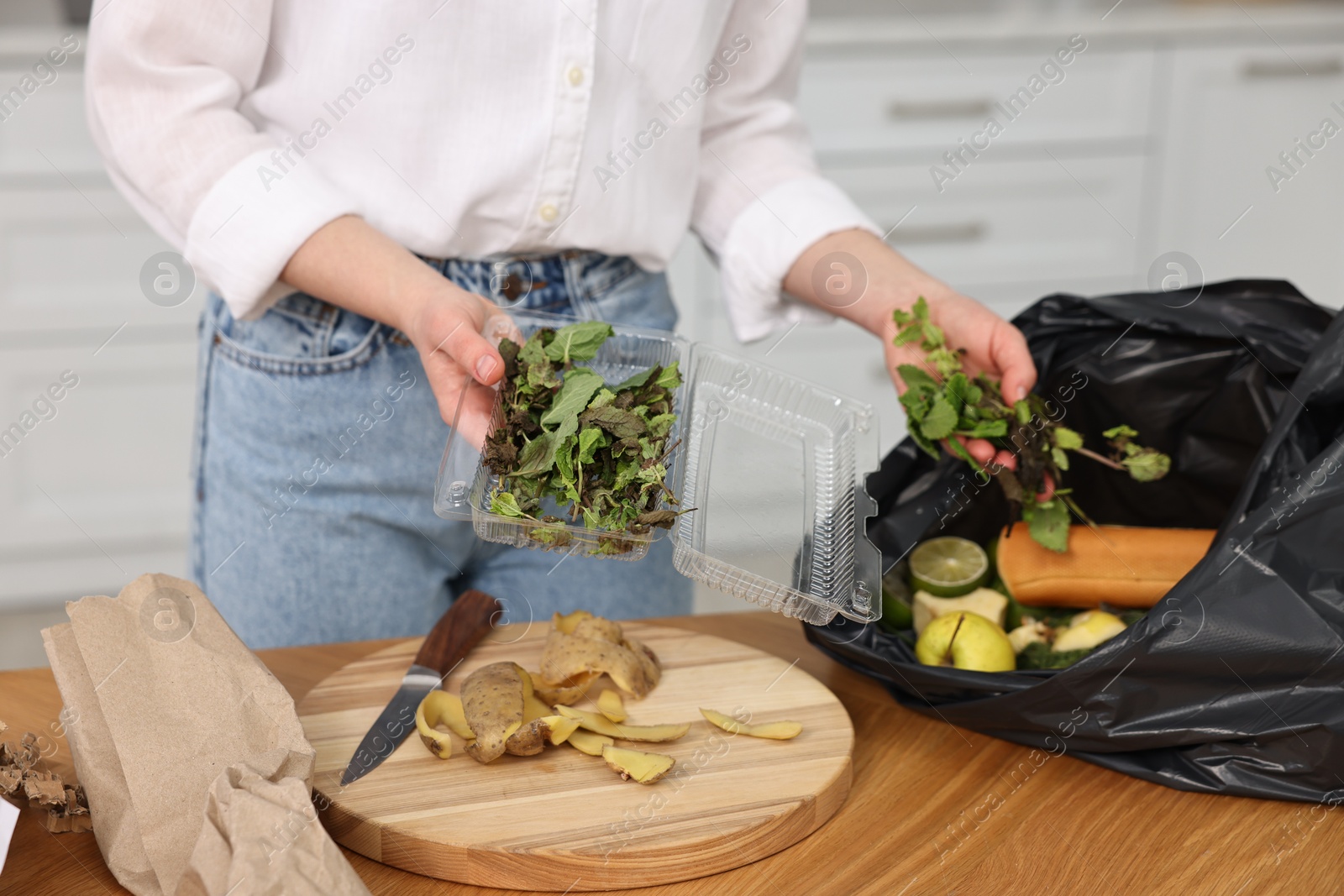 Photo of Garbage sorting. Woman putting food waste into plastic bag at wooden table indoors, closeup