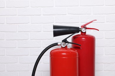 Red fire extinguishers near white brick wall, space for text