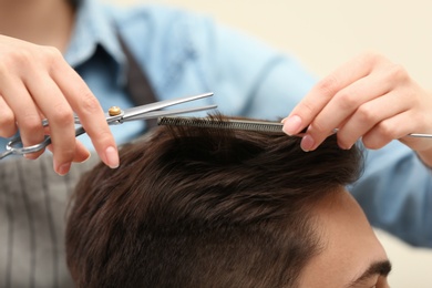 Barber making stylish haircut with professional scissors in beauty salon, closeup