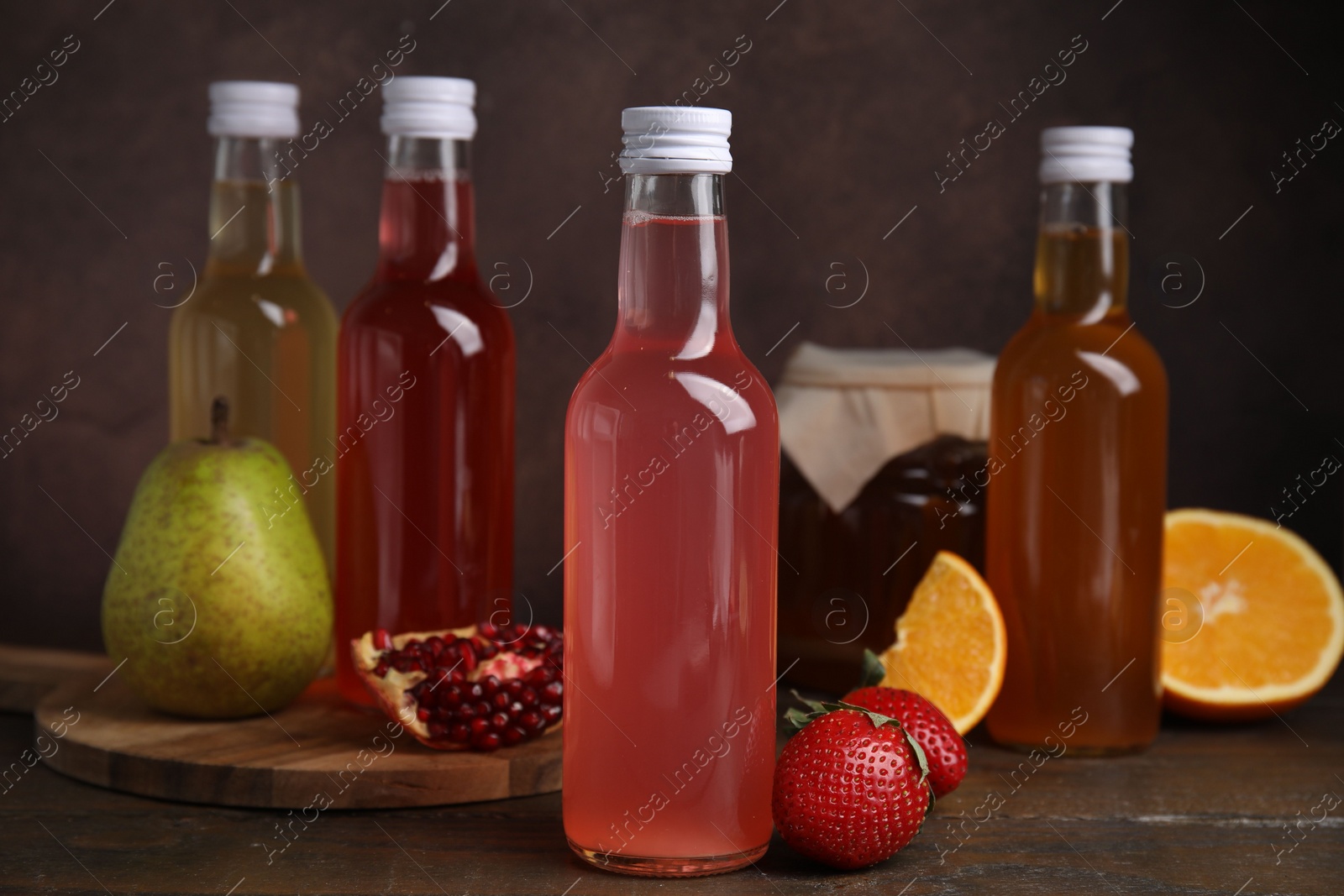 Photo of Delicious kombucha in glass bottles, jar and fresh fruits on wooden table