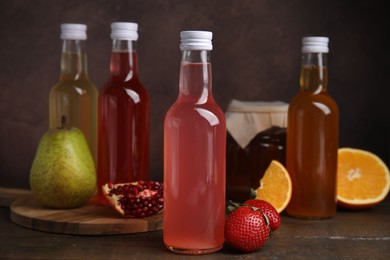 Photo of Delicious kombucha in glass bottles, jar and fresh fruits on wooden table