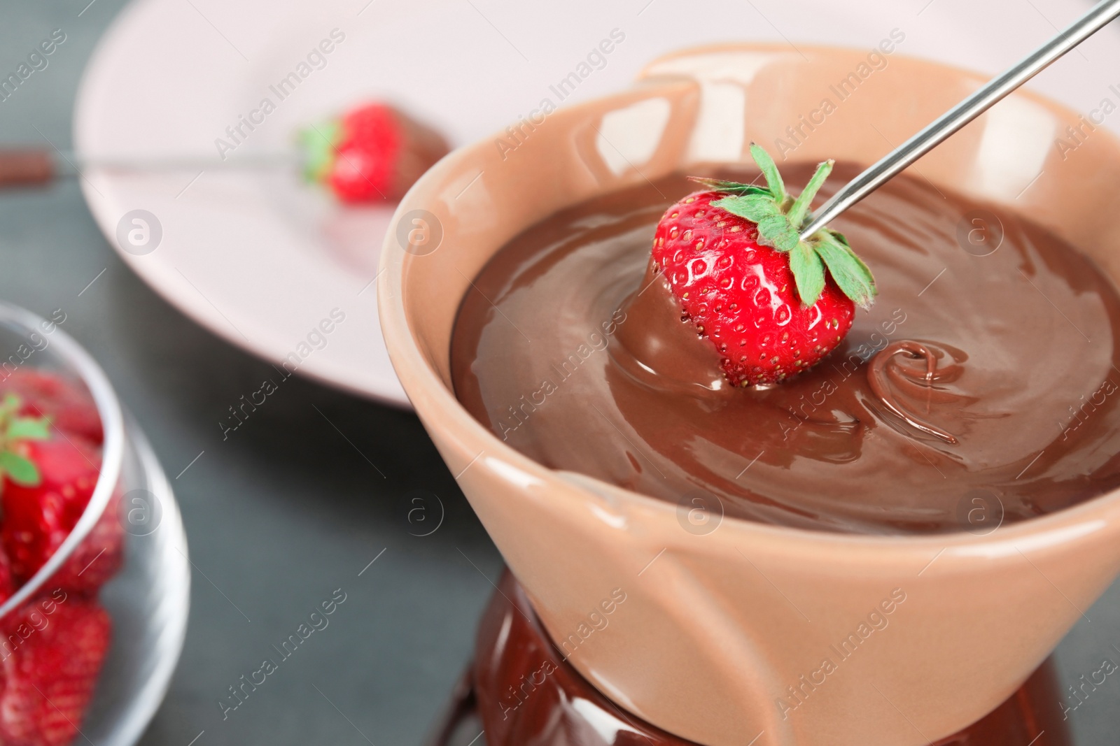 Photo of Ripe strawberry dipping into chocolate fondue, closeup