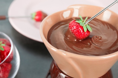 Photo of Ripe strawberry dipping into chocolate fondue, closeup