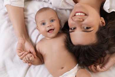 Photo of Happy young mother with her cute baby on bed, top view