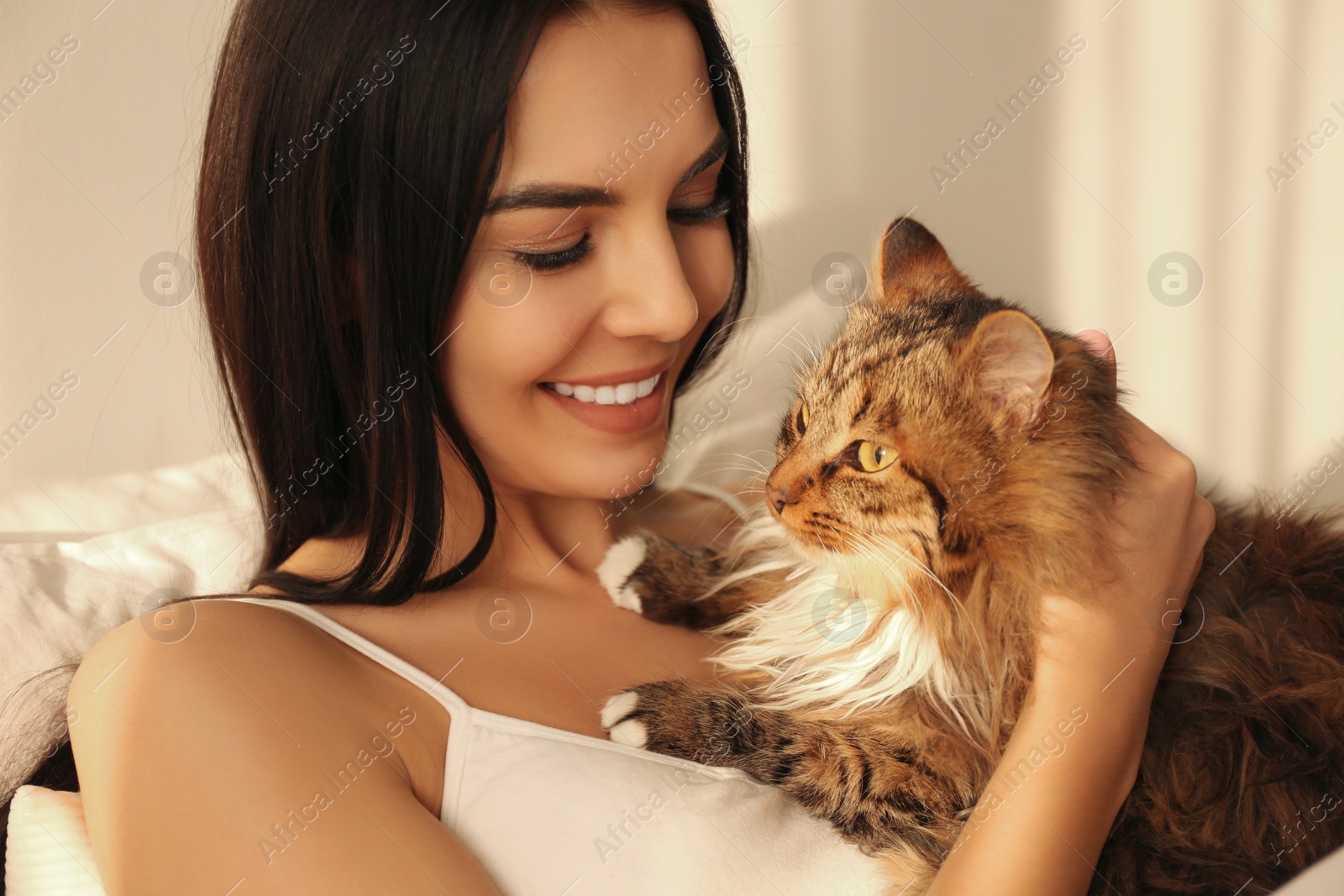 Photo of Beautiful young woman with her cute cat on bed. Fluffy pet