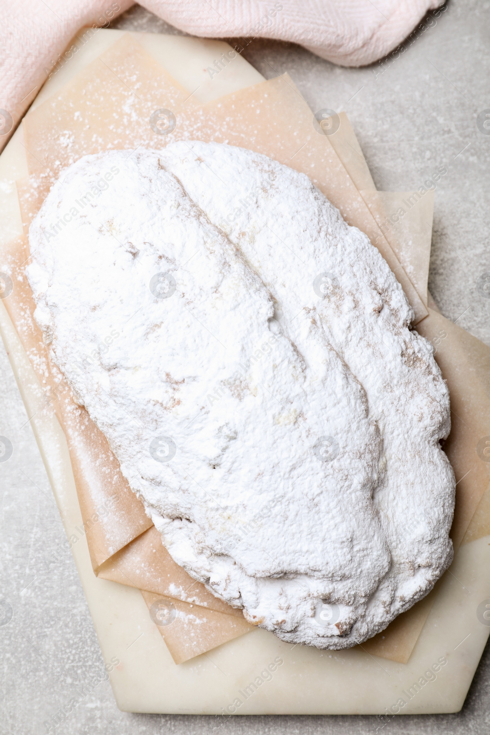 Photo of Delicious Stollen sprinkled with powdered sugar on light table, top view