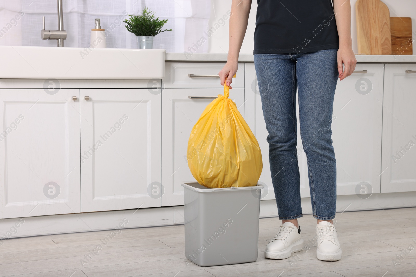 Photo of Woman taking garbage bag out of trash bin in kitchen, closeup. Space for text