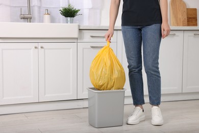 Photo of Woman taking garbage bag out of trash bin in kitchen, closeup. Space for text