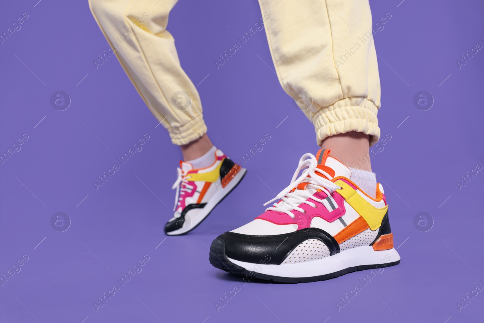 Photo of Woman wearing pair of new stylish sneakers on purple background, closeup