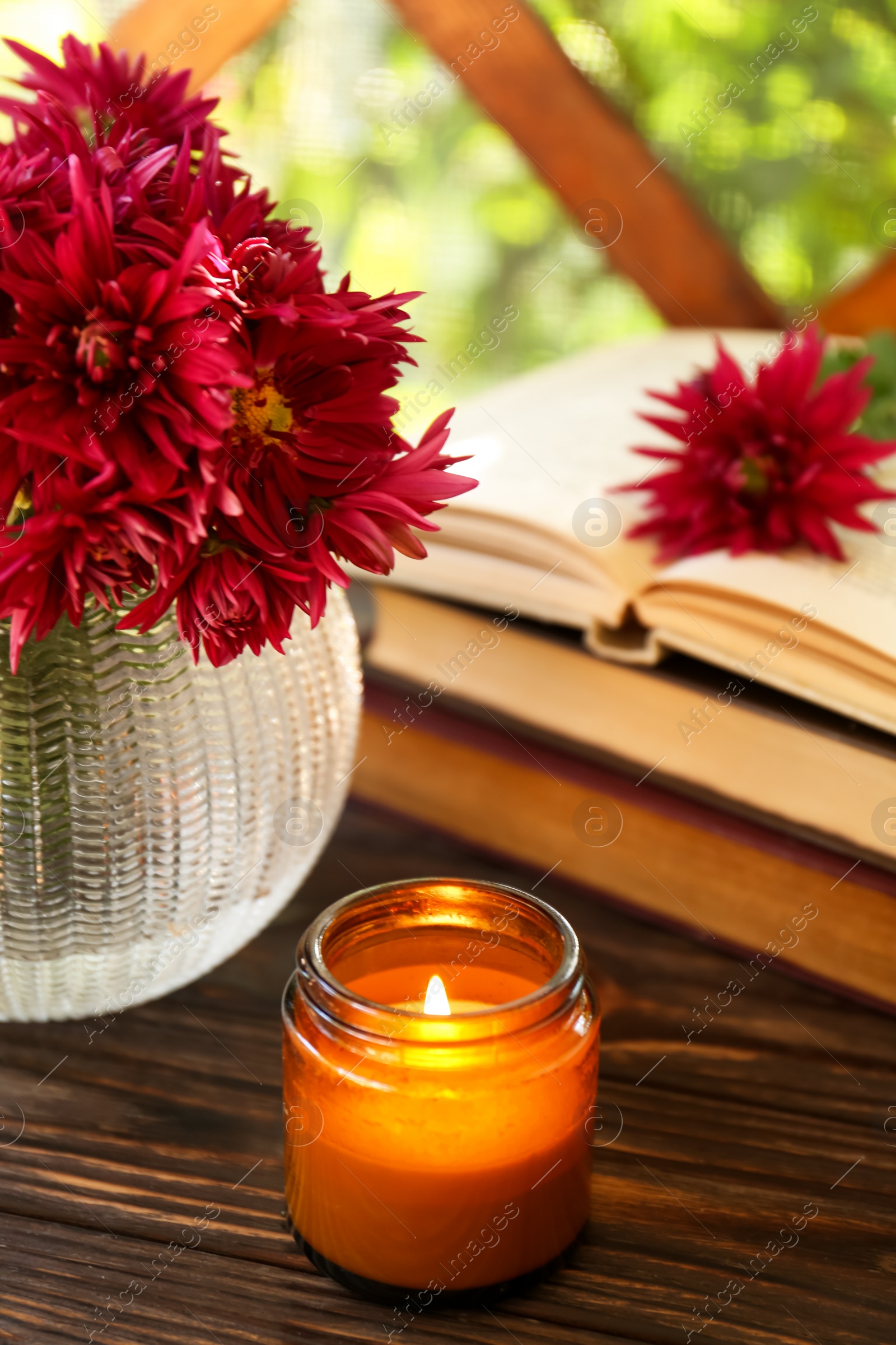 Photo of Beautiful pink chrysanthemum flowers, burning candle and books on wooden table