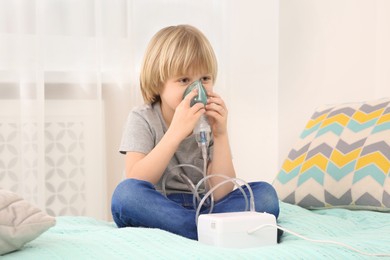 Sick little boy using nebulizer for inhalation on bed at home