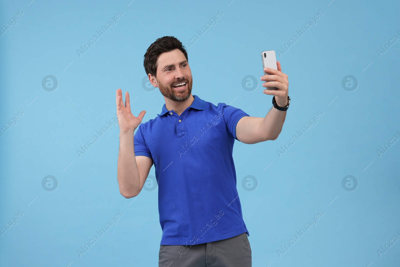 Photo of Smiling man taking selfie with smartphone on light blue background