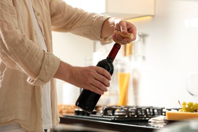 Man opening wine bottle with corkscrew indoors, closeup. Space for text