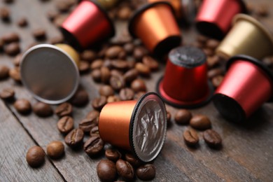 Many coffee capsules and beans on wooden table, closeup