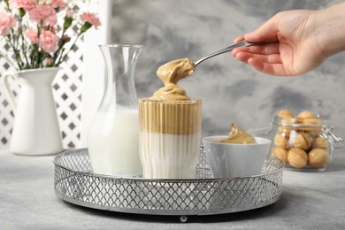 Photo of Woman pouring cream for dalgona coffee into glass at light grey table, closeup