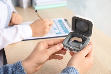 Photo of Patient with hearing aid in box and blurred doctor on background, closeup