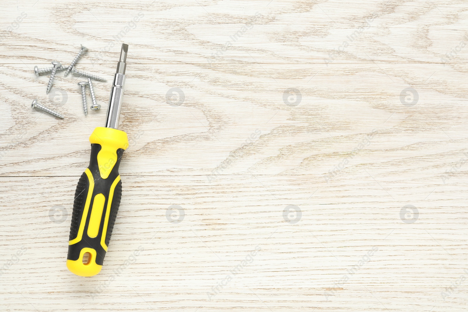 Photo of Screwdriver with yellow handle and screws on white wooden table, flat lay. Space for text