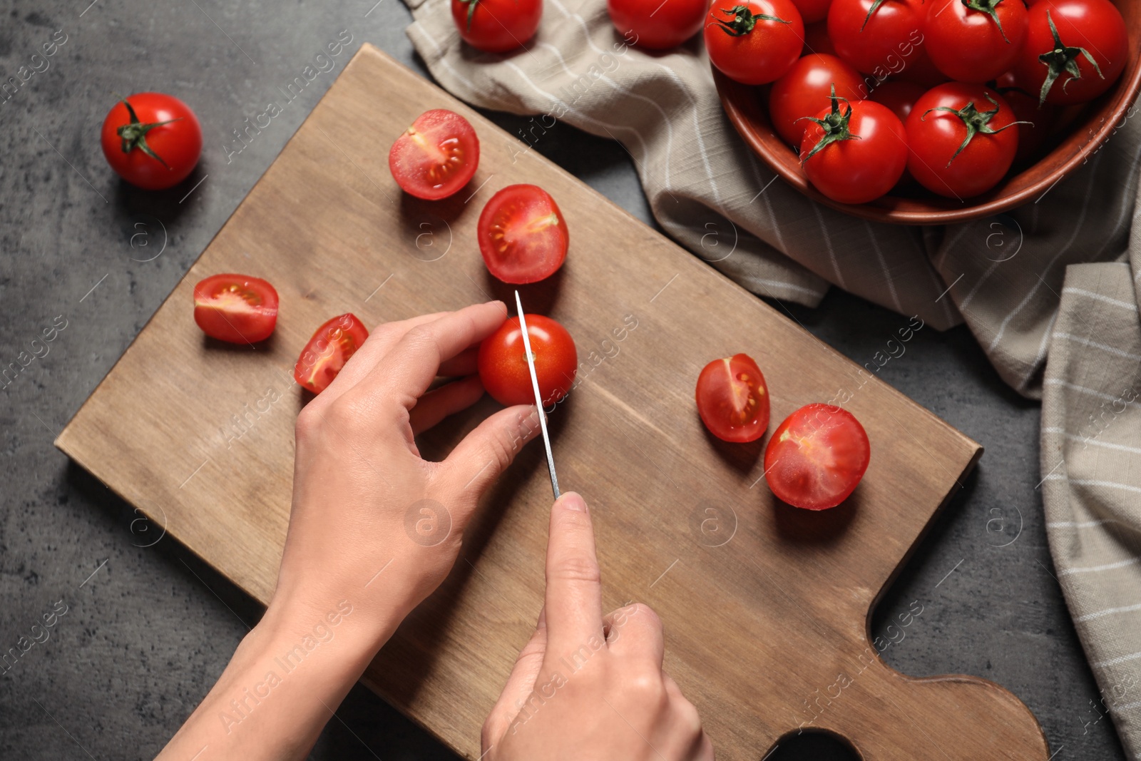 Photo of Woman cutting fresh cherry tomatoes on wooden board at table, top view