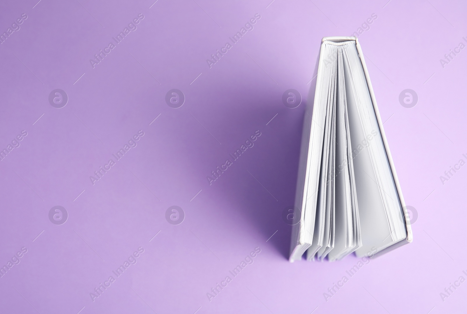 Photo of Hardcover book on violet background, top view. Space for text