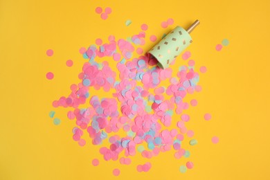 Party popper with bright confetti on orange background, flat lay
