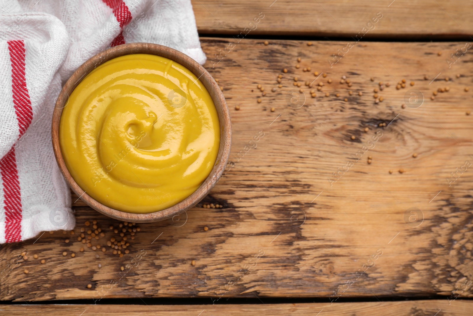 Photo of Sauce bowl with delicious mustard and seeds on wooden table, flat lay. Space for text