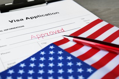 Photo of Visa application form with word Approved, American flag and pen on table, closeup