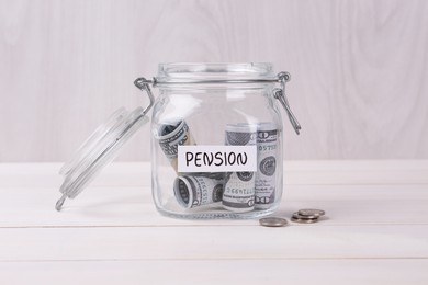 Glass jar with word Pension, coins and dollar banknotes on white wooden table