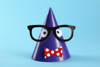 Photo of Handmade party hat with funny face on light blue background
