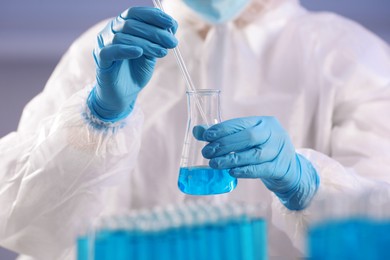 Scientist taking sample of light blue liquid on grey background, closeup