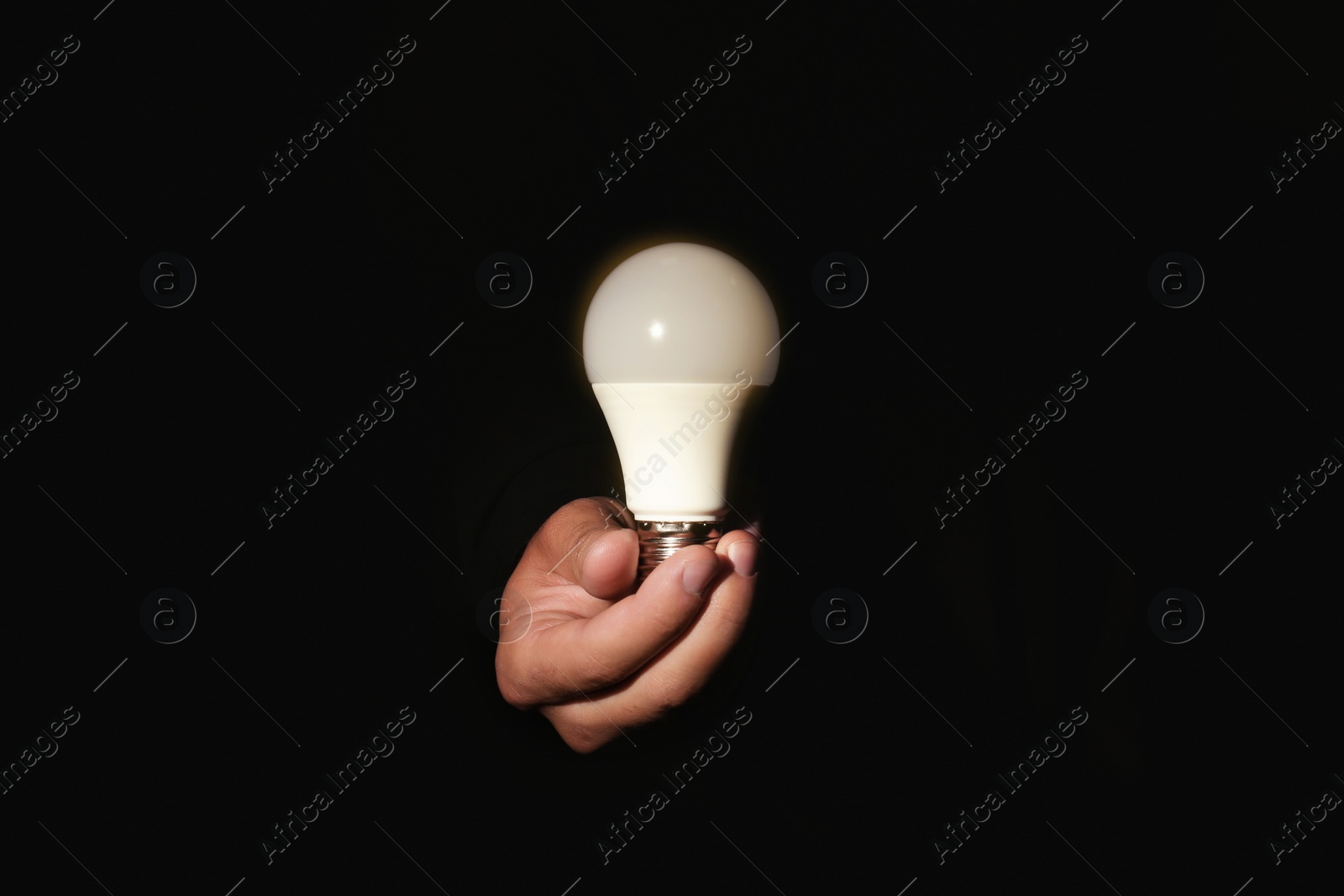 Photo of Man holding modern lamp bulb on dark background, closeup