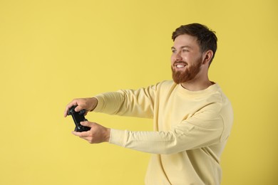 Photo of Happy man playing video game with controller on pale yellow background