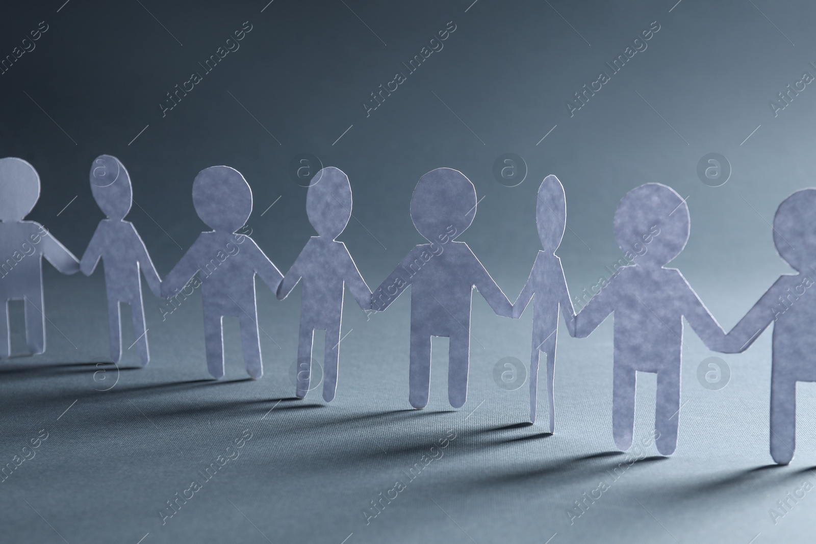 Photo of Teamwork concept. Paper figures of people holding hands on grey background, closeup