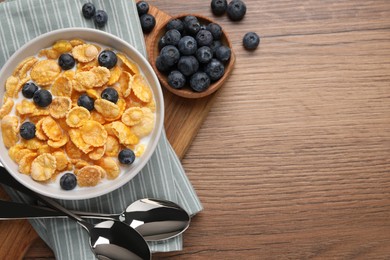 Bowl of tasty crispy corn flakes with milk and blueberries on wooden table, flat lay. Space for text