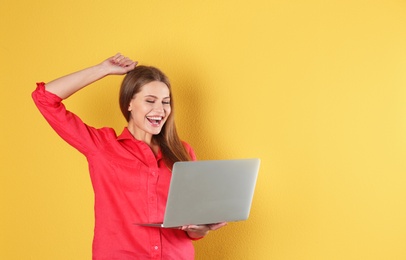 Emotional young woman with laptop celebrating victory on color background. Space for text