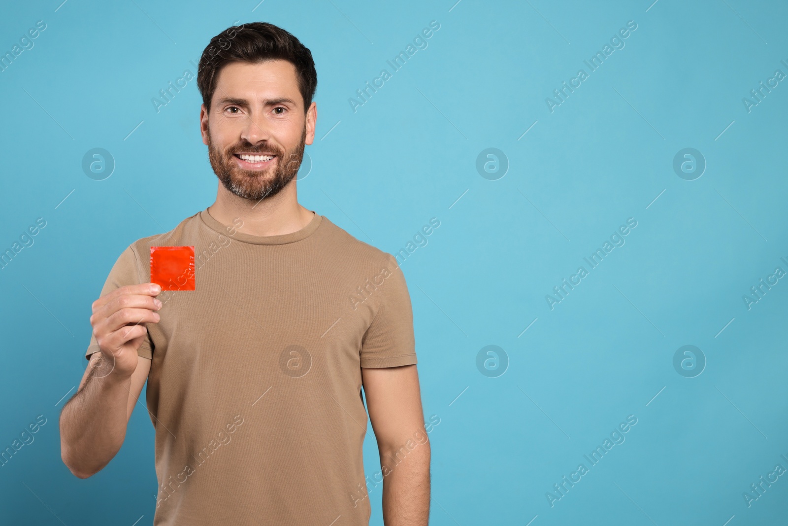 Photo of Happy man holding condom on light blue background, space for text. Safe sex