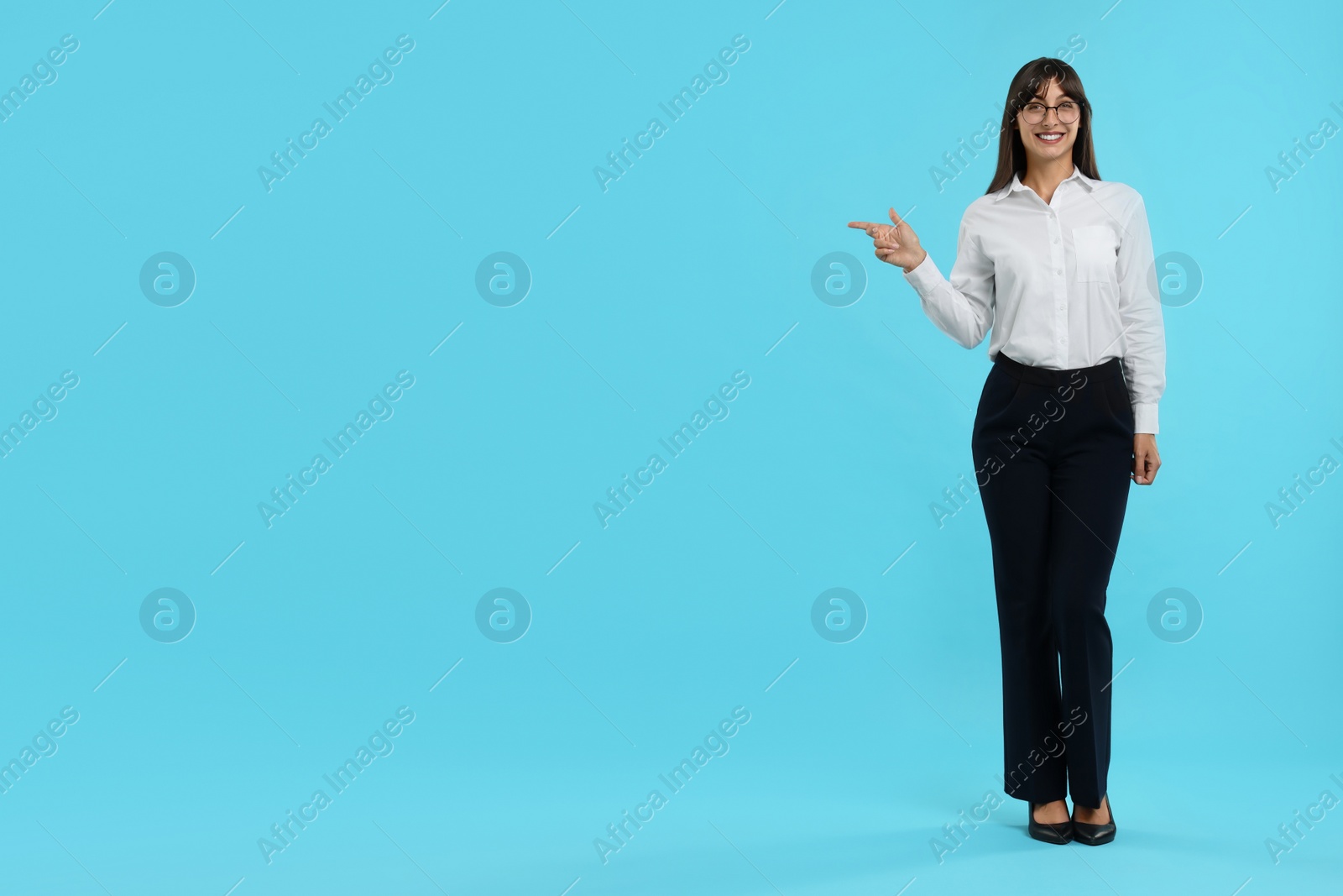 Photo of Happy secretary pointing at something on light blue background. Space for text