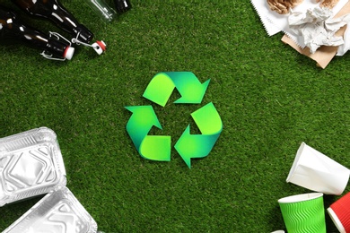 Photo of Flat lay composition with recycling symbol and different garbage on green grass