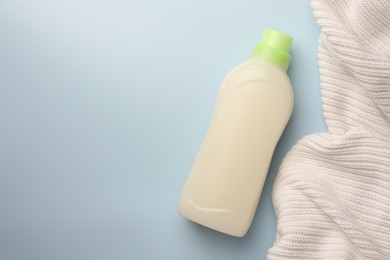 Photo of Bottle of fabric softener and white knitted cloth on light background, flat lay. Space for text