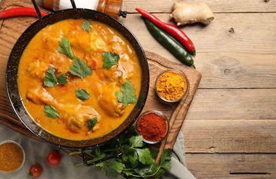 Photo of Tasty chicken curry with parsley and ingredients on wooden table, flat lay. Space for text
