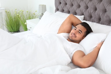 Photo of Young man lying in bed with soft pillows at home