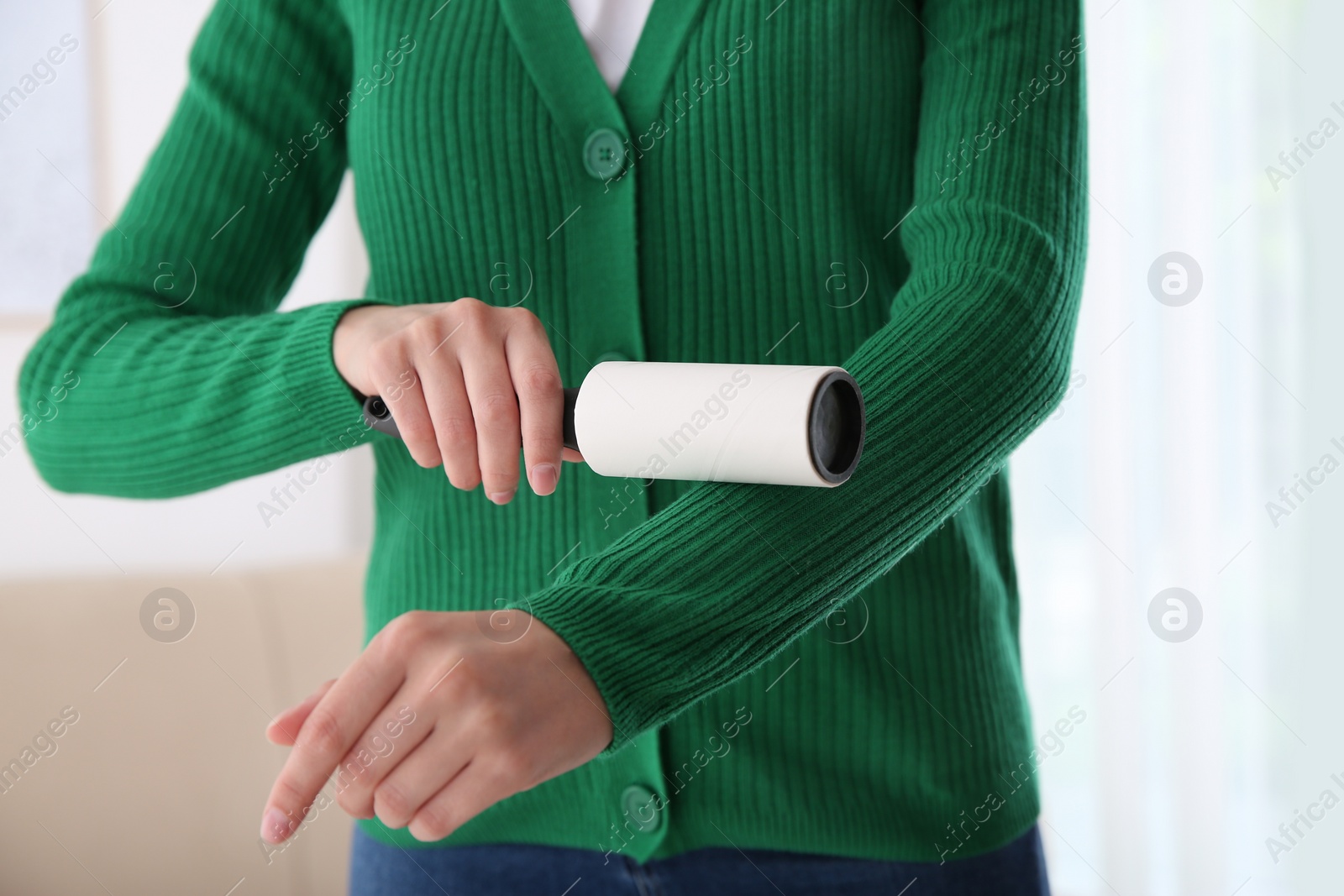 Photo of Woman cleaning green jacket with lint roller indoors, closeup