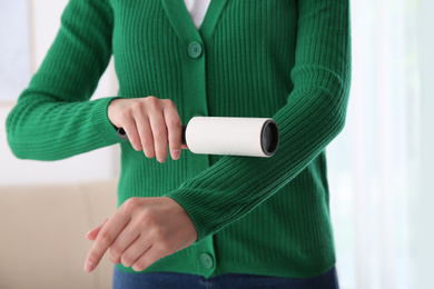 Woman cleaning green jacket with lint roller indoors, closeup