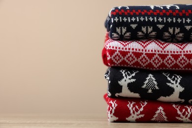 Photo of Stack of different Christmas sweaters on beige background, closeup. Space for text