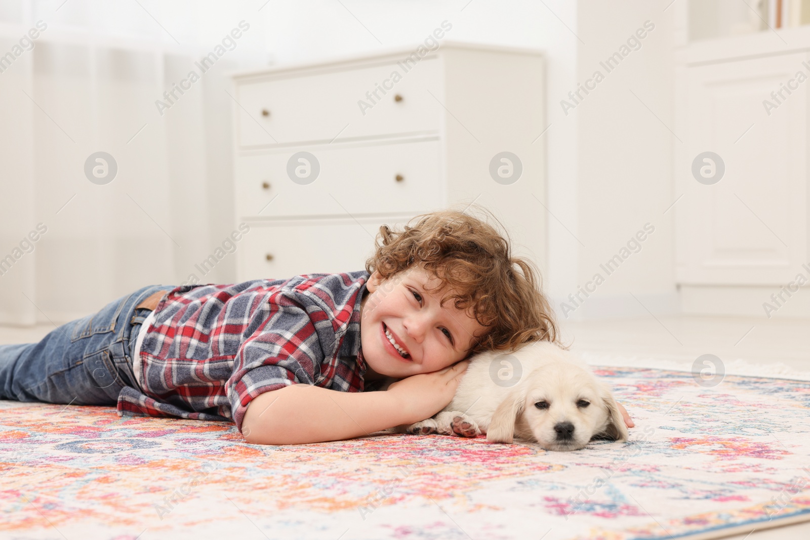 Photo of Little boy lying with cute puppy on carpet at home