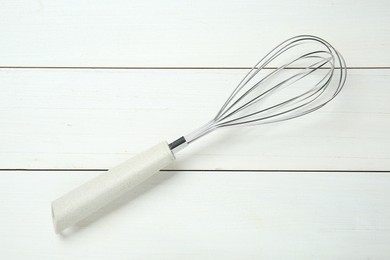 Metal whisk on white wooden table, top view