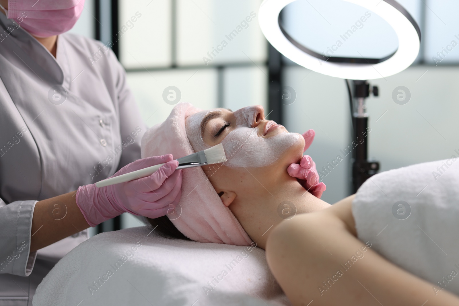 Photo of Cosmetologist applying mask on woman's face in clinic, closeup