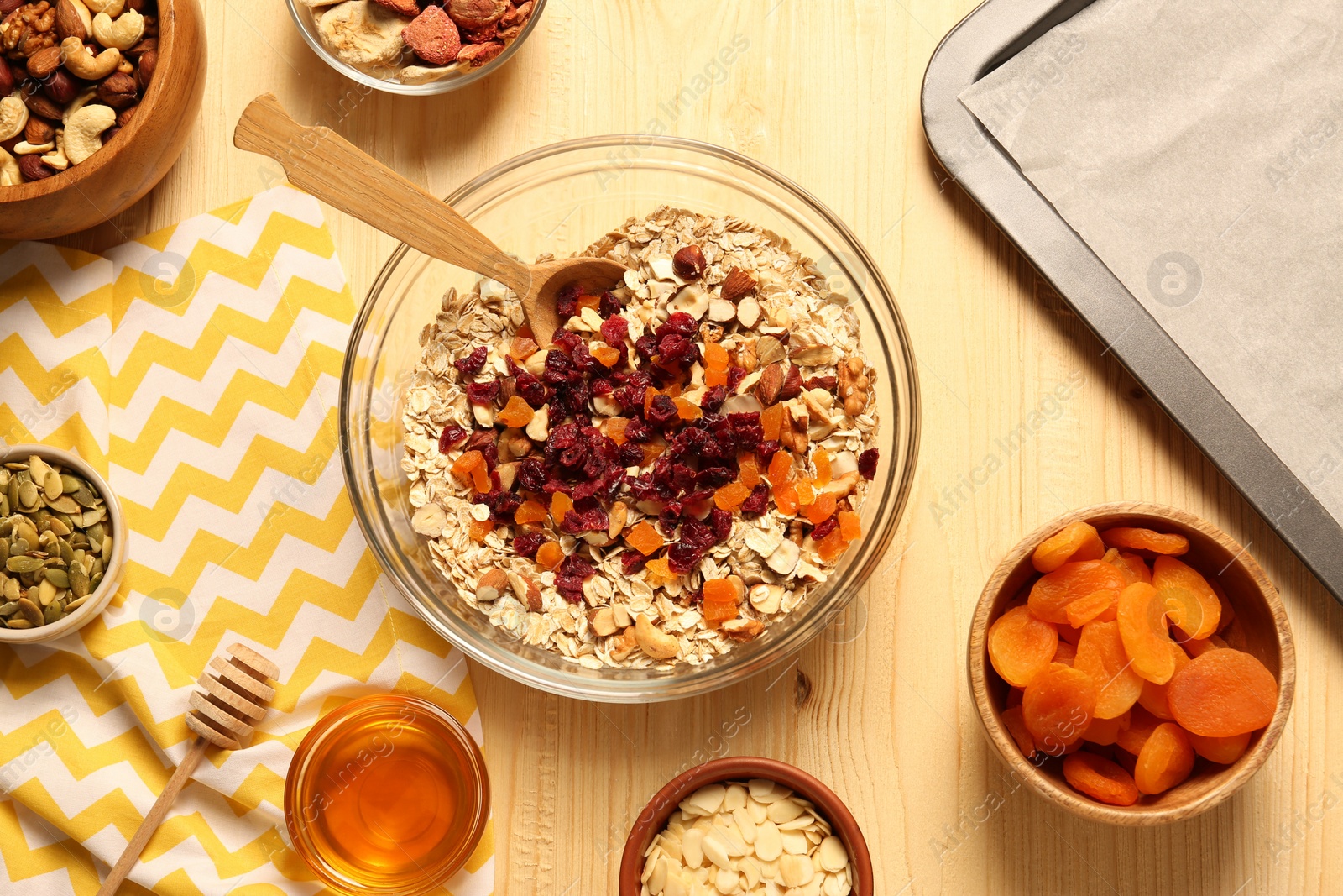 Photo of Making granola. Oat flakes, dried apricots and other ingredients on wooden table, flat lay