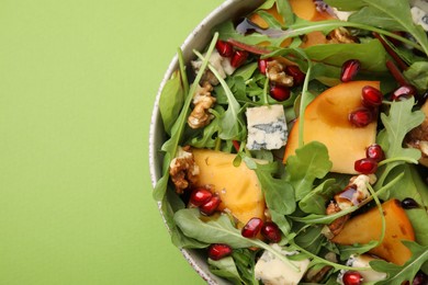 Photo of Tasty salad with persimmon, blue cheese, pomegranate and walnuts served on light green background, top view. Space for text